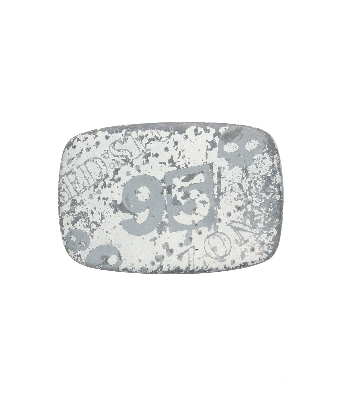 A rectangular, weathered metal object—a rugged buckle by Bed|Stü called the "95 Buckle"—features faded white numbers, including a prominent "95," along with indistinct text and patterns.