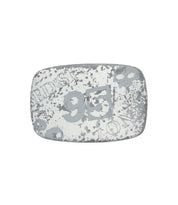 A rectangular, weathered metal object—a rugged buckle by Bed|Stü called the "95 Buckle"—features faded white numbers, including a prominent "95," along with indistinct text and patterns.