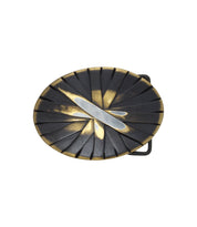 The Brit Oval Buckle by Bed|Stü features an oval metal design with a dark, ridged background and a silver diagonal stripe across the center, offering a textured look reminiscent of an antiqued bronze buckle.