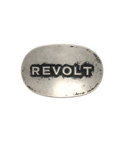 Bed|Stü’s Revolt Buckle features an oval silhouette and a silver-tone finish, with “REVOLT” boldly engraved in uppercase letters; its worn, aged surface enhances the buckle’s unmistakable punk and rebellious appeal.