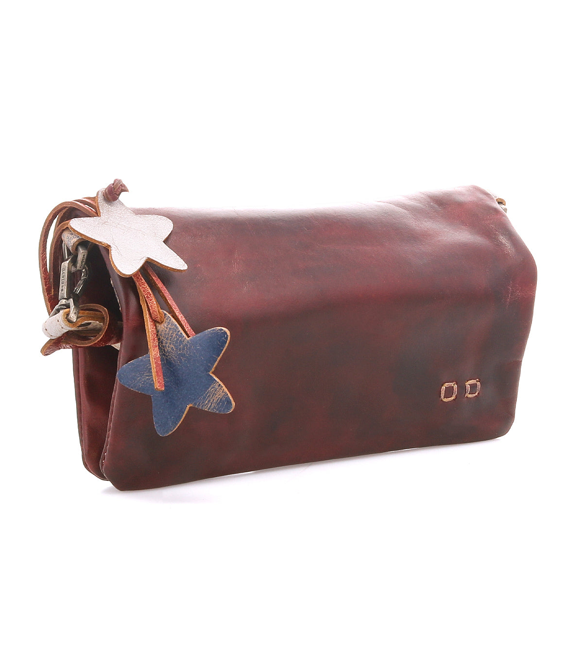 Introducing Cadence by Bed|Stü: a brown crossbody clutch bag, exquisitely crafted from vegetable-tanned leather and adorned with two star-shaped charms—one white and one blue—gracefully attached to the side.