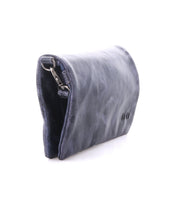 The Bed|Stü Cadence is a dark blue, vegetable-tanned leather pouch featuring a metal clasp, photographed against a white background with the image highlighting its side profile and partially revealing the interior.