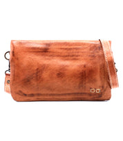 The Cadence crossbody clutch by Bed|Stü is a rectangular brown bag crafted from premium vegetable-tanned leather, featuring a long strap and a small metallic logo detail in the bottom right corner.