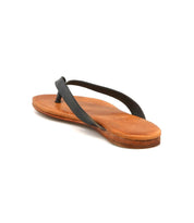 The Bed|Stü Calma sandal, featuring a flat sole and thin black straps, is displayed in brown leather on a white background and viewed from a rear diagonal angle.