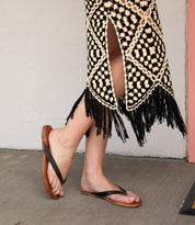 Wearing the Calma lightweight brown leather sandals by Bed|Stü, paired with a black and beige crochet skirt with fringe, standing comfortably on a concrete floor.