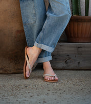 A person wearing rolled-up blue jeans and comfortable Calma beige flip-flops by Bed|Stü stands on a concrete surface next to a potted plant.