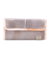 The Bed|Stü Canton is a gray leather wallet featuring a tan trim and a small rectangular patch on the lower right corner, designed as a sleek 2-in-1 clutch, shown against a white background.