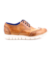 The Cayuga II by Bed|Stü are brown leather derby shoes with classic brogue detailing and a wingtip design, featuring a white rubber sole, blue inner lining, and decorative perforations, shown in profile on a white background.