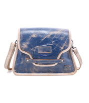 The Bed|Stü Ceremonious is a blue and tan leather preppy flap-top bag featuring visible stitching, an adjustable shoulder strap, and a magnetic closure. Its organized interior provides convenient storage for your essentials.