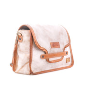 The Bed|Stü Ceremonious is a tan and brown preppy flap-top leather bag featuring a magnetic flap closure, side metal rings, and a small rectangular logo patch on the front. Its thoughtfully designed interior keeps your essentials neatly organized.