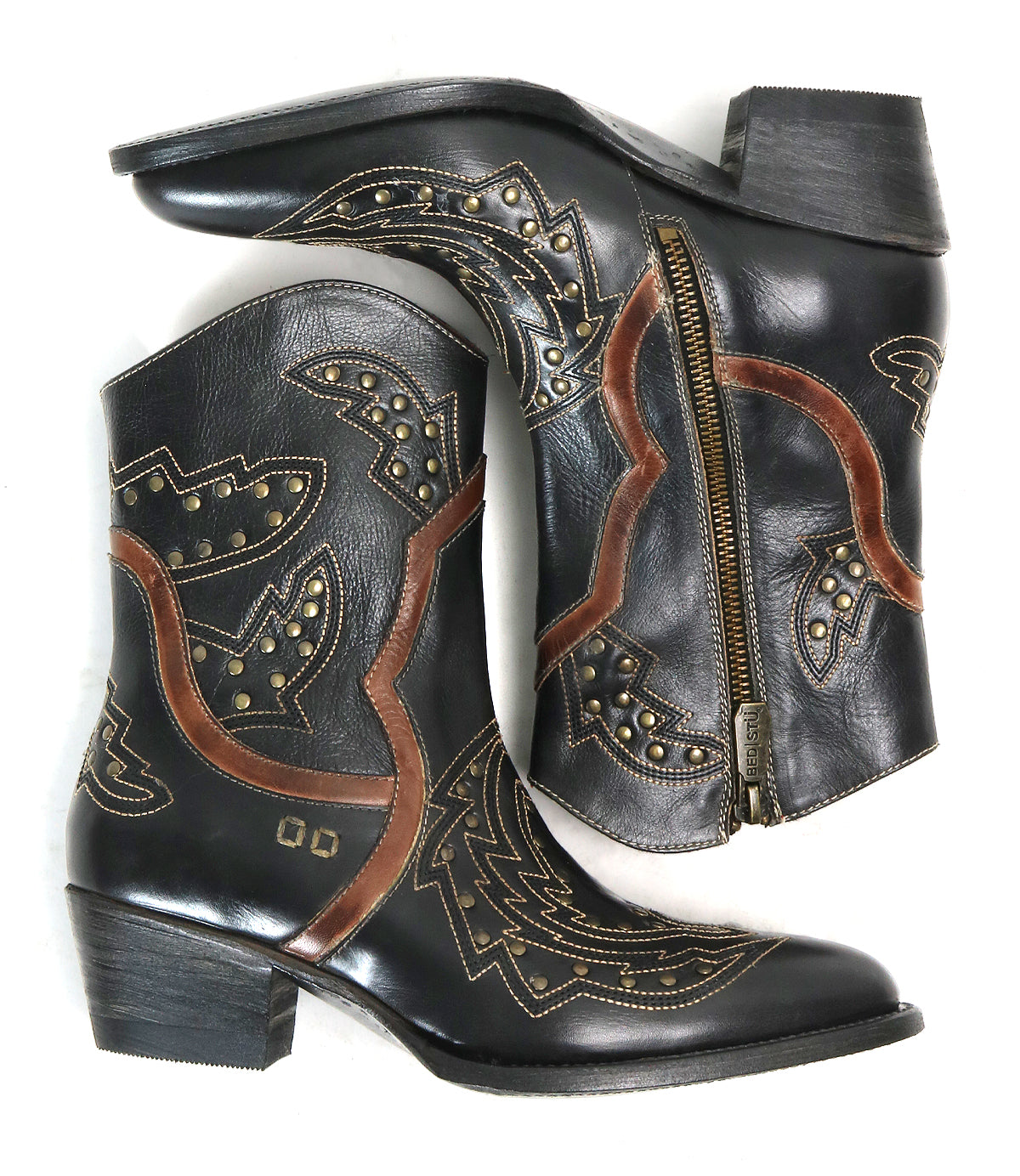 A pair of Chamise black leather ankle boots by Bed|Stü, featuring brown and gold decorative stitching, stud accents, and side zippers, are arranged overlapping on a white background—these stylish western boots offer a modern take on the classic mid-height boot silhouette.