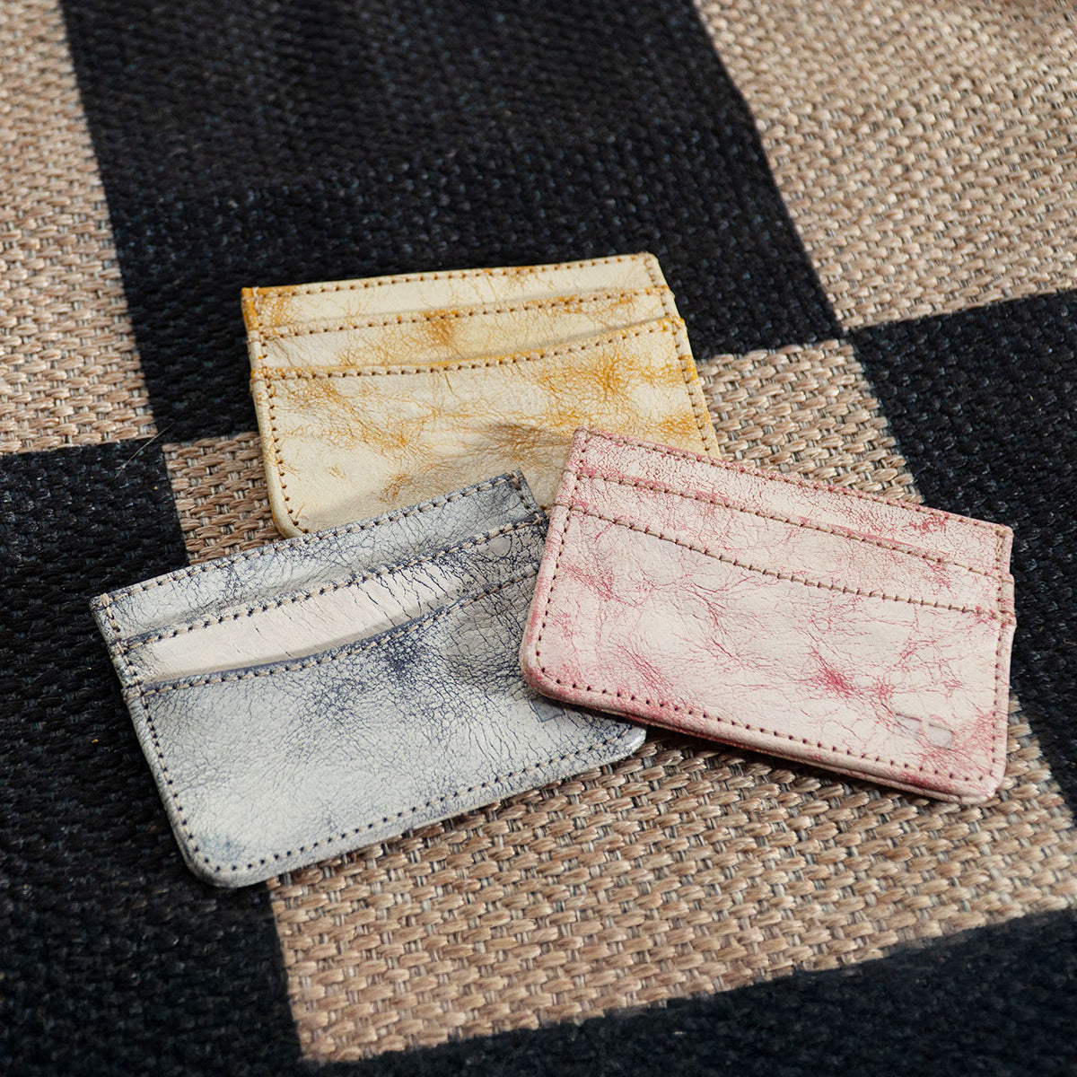 Three Chuck small leather cardholders by Bed|Stü—perfect as slim wallets or compact card holders in yellow, blue, and pink—are placed on a woven checkered surface, making them ideal for your everyday carry.