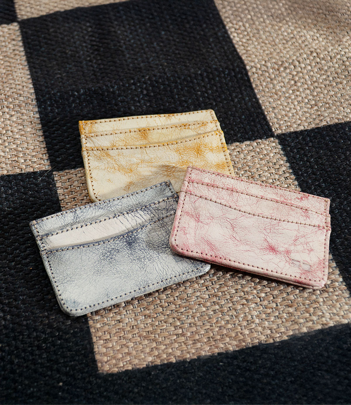 Three Chuck small leather cardholders by Bed|Stü—perfect as slim wallets or compact card holders in yellow, blue, and pink—are placed on a woven checkered surface, making them ideal for your everyday carry.