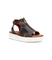 The Bed|Stü Clancy is an open-toe brown sandal, crafted from stylish cutout leather with a front zipper, ankle strap, and metallic rivets. It features a thick white ridged sole and cushioned insole for all-day comfort, shown against a white background.