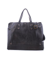 The Bed|Stü Commuter is a black leather bag featuring two handles, an adjustable shoulder strap, metal hardware, and decorative stitching along the bottom edge, displayed against a white background.