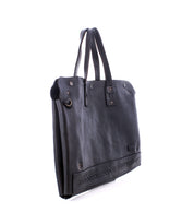 The Bed|Stü Commuter is a black leather tote bag with two handles, decorative stitching near the base, and metal hardware accents, shown on a white background. Perfect as a mobile office or commuter bag, it blends style and practicality for your on-the-go lifestyle.