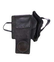 Bed|Stü Commuter bag in black leather, featuring a flap open to reveal multiple compartments and a round patch on one side, photographed against a white background.