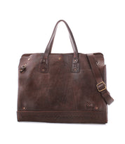 The Bed|Stü Commuter is a brown leather tote bag featuring dual handles, a detachable shoulder strap, brass hardware, and decorative stitching along the bottom edge—ideal as a stylish commuter bag or an elegant laptop bag for your everyday needs.
