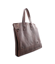 The Bed|Stü Commuter is a brown leather bag featuring two handles, decorative stitching near the base, metal rivets, and a classic rectangular shape. Photographed against a white background, this bag offers both style and functionality—making it an excellent choice for anyone in need of a sophisticated laptop carrier.