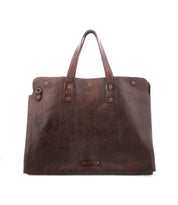 The Bed|Stü Commuter is a large, rectangular brown leather bag featuring two sturdy handles and metal rivet detailing, ideal for carrying your essentials as a stylish laptop or mobile office bag. Shown against a white background.