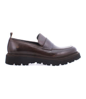The Bed|Stü Costruito, an Italian-made penny loafer in brown vegetable-tanned leather, is displayed in profile against a white background, highlighting its thick black Livetech outsole for a contemporary touch.