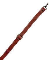 The Bed|Stü Crossbody Strap features a brown leather adjustable design with a brass buckle and metal clasp, displayed diagonally on a white background—ideal as an adjustable leather strap for Bed|Stü bags or as a fashionable crossbody accessory.