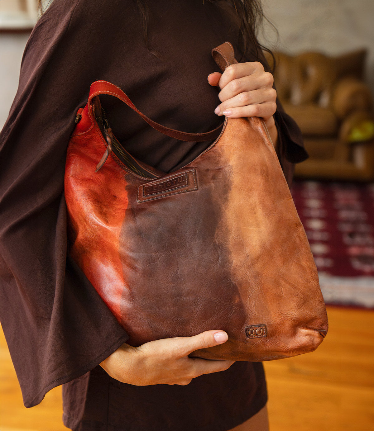 A person holds a slouchy, multicolored Bed|Stü Dallas LTC shoulder bag featuring tones of red, brown, and tan.