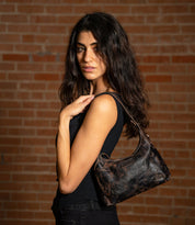 A woman carries a small, dark, vegetable-tanned leather Bed|Stü Denton hobo bag over her shoulder.