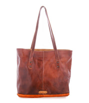The Bed|Stü Dome is a brown leather tote bag featuring two shoulder straps, visible stitching, and a small gold-colored logo plate near the bottom center front. With its spacious interior, the Dome is perfect for carrying your work essentials in style.