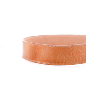 A close-up of the Dreampath EM by Bed|Stü, a round, light brown leather container featuring intricate floral embossing and expertly crafted from the same genuine leather found in modern style belts celebrated for their rugged durability. The piece is showcased against a white background.