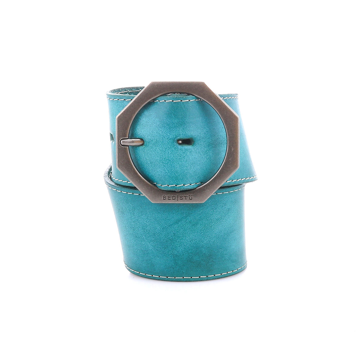 The Bed|Stü Dreampath is a wide turquoise genuine leather belt featuring visible stitching and a large round octagonal metal buckle, artistically rolled up on a white background. This accessory showcases the brand’s commitment to quality craftsmanship and distinctive style.