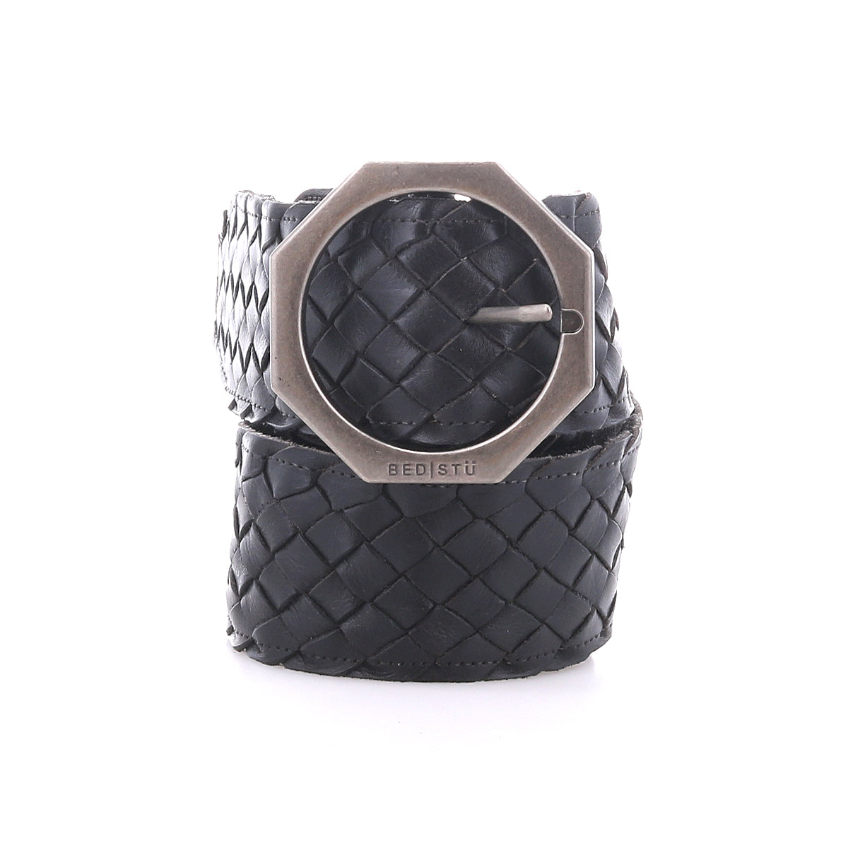 The Dreamweaver by Bed|Stü is a black woven leather belt featuring a prominent hexagonal silver buckle engraved with “BED|STU,” masterfully crafted and presented rolled up against a white background.