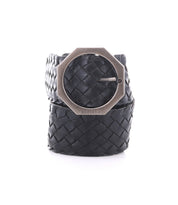 The Dreamweaver by Bed|Stü is a black woven leather belt featuring a prominent hexagonal silver buckle engraved with “BED|STU,” masterfully crafted and presented rolled up against a white background.