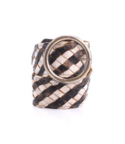 The Bed|Stü Dreamweaver is a woven leather belt in a black and white checker pattern, highlighting artisan craftsmanship with a large round silver buckle, shown rolled up on a white background.