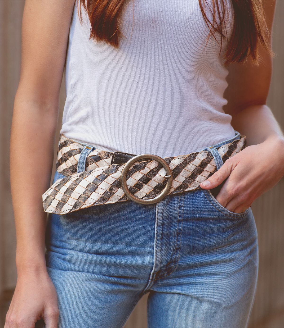 Wearing the Bed|Stü Dreamweaver—a woven leather belt with a large round buckle—paired with a white tank top and blue jeans, this person keeps one hand in their pocket for a perfect touch of bohemian style.