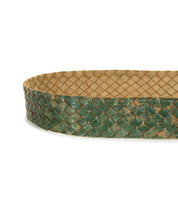 A close-up of the Bed|Stü Dreamweaver, a green woven leather belt with a tan inner lining, beautifully showcases artisan craftsmanship. The belt is arranged in an oval shape against a white background.