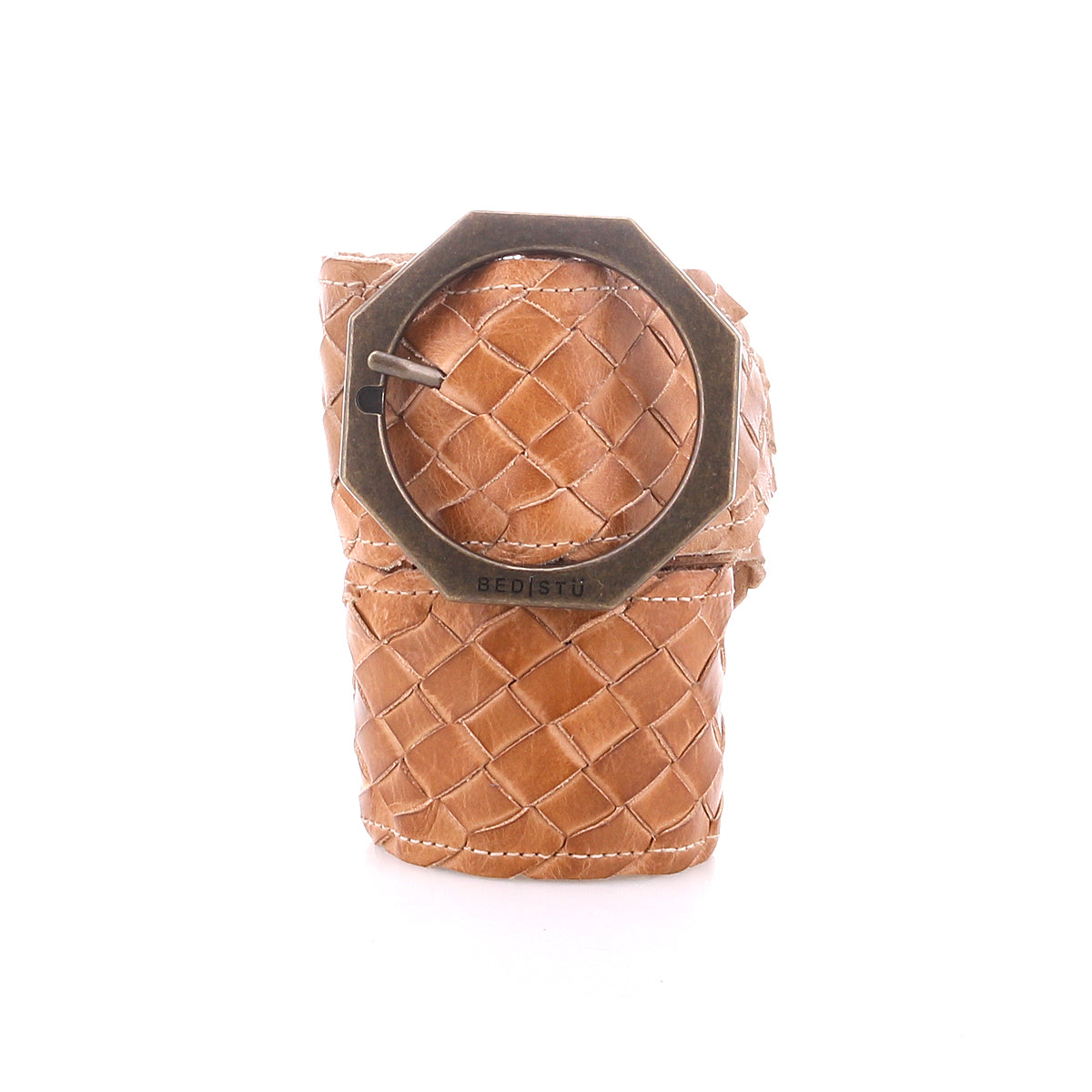 The Dreamweaver napkin ring by Bed|Stü features tan woven leather, reminiscent of a finely crafted belt, and is accented with an octagonal metal buckle engraved with "BED|STÜ." Showcasing artisan craftsmanship and subtle bohemian style, it is displayed on a plain white background.