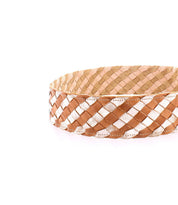 The Dreamweaver basket by Bed|Stü is a round, shallow piece featuring a woven pattern in tan, brown, and white, showcasing artisan craftsmanship against a plain white background.