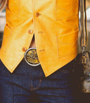 Wearing the Bed|Stü Dreamweaver yellow leather vest, dark blue jeans, an artisan-crafted patterned belt buckle, and carrying a brown leather purse creates an effortlessly bohemian look.
