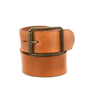 The Drifter belt by Bed|Stü is a tan textured leather strap, rolled up and featuring a rectangular metal buckle, showcased in a minimal style against a white background.