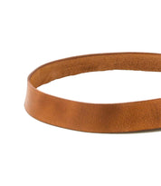 The Drifter belt by Bed|Stü is displayed in a circular shape on a white background, highlighting its minimal style and subtly textured brown leather strap with a classic metal buckle.