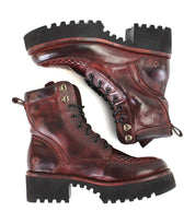 A pair of Bed|Stü Elisha Hi boots in rugged dark red leather, featuring a classic lace-up profile with metal eyelets and thick black treaded soles, are placed side by side against a white background.