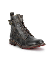 The Bed|Stü Endure is a single black leather lace-up boot with a textured finish, side buckle strap, and low heel, displayed on a white background. This rugged leather boot features a durable treaded outsole for enhanced grip and long-lasting wear.
