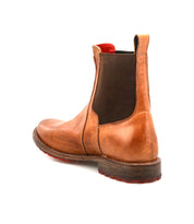 The Bed|Stü Ethic is a durable brown Chelsea boot featuring a leather lining, dark elastic side panel, distinctive red outsole, and a wooden heel, displayed from the rear angle against a white background.