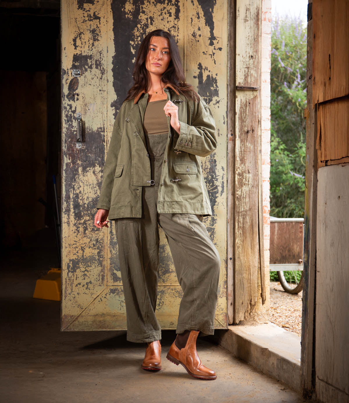 A woman stands in a doorway with one hand in her pocket, her neutral expression effortlessly highlighting the Ethic Chelsea boots by Bed|Stü, featuring a durable design and leather-lined finish.
