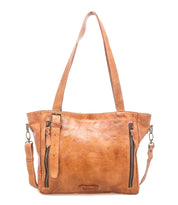 Crafted by Bed|Stü, the Explicit LTC is a light brown leather handbag featuring dual shoulder straps, front zipper pockets, a detachable crossbody strap, and a small decorative buckle detail on the front—combining rustic charm with reliable everyday function for effortless style.