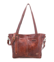 Meet the Explicit LTC by Bed|Stü—a brown leather shoulder bag featuring two sturdy handles, an adjustable strap, and a front pocket. Visible stitching and a small embossed Bed|Stü logo enhance its rustic charm. Designed for everyday dependability, this piece stands out beautifully against a plain white background.