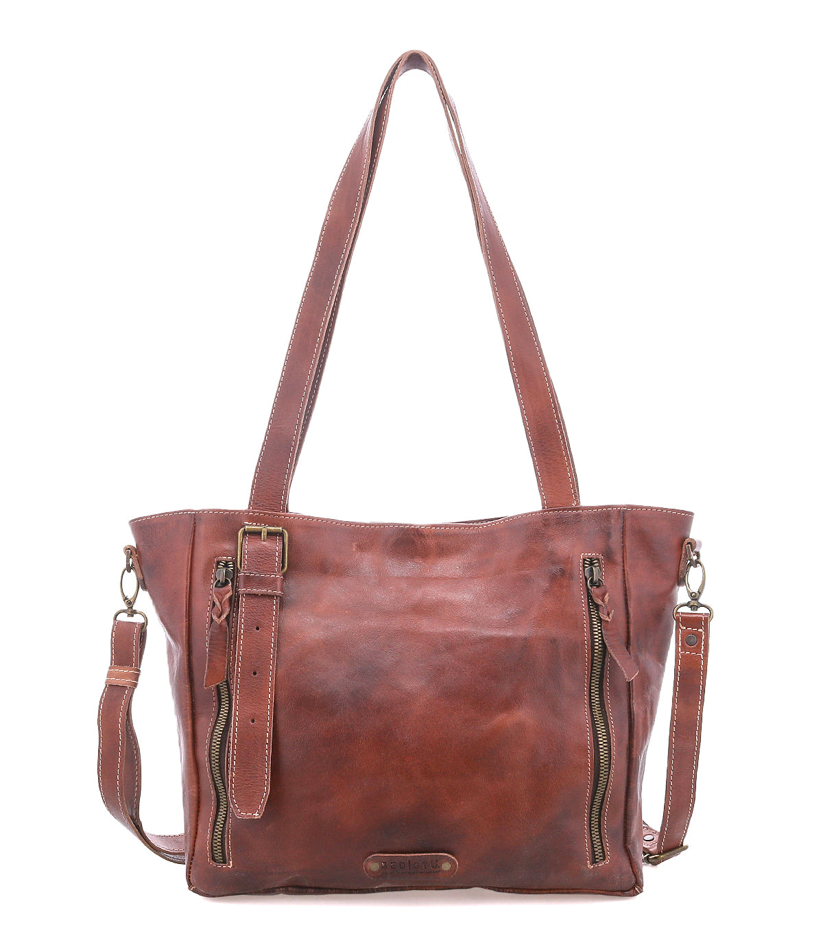 The Bed|Stü Explicit LTC is a brown leather tote bag featuring two vertical front zippers, dual shoulder straps, a detachable long strap, and visible stitching for rustic appeal and everyday dependability.
