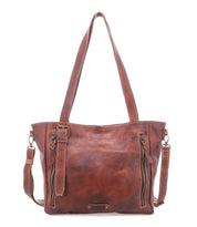 The Bed|Stü Explicit LTC is a brown leather tote bag featuring two vertical front zippers, dual shoulder straps, a detachable long strap, and visible stitching for rustic appeal and everyday dependability.
