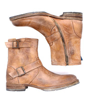 Bed|Stü's Fellow is a pair of brown leather ankle boots featuring Goodyear welt construction, side zippers, and buckle straps—a rugged staple inspired by classic moto boot design. One boot lies flat while the other rests on its side.